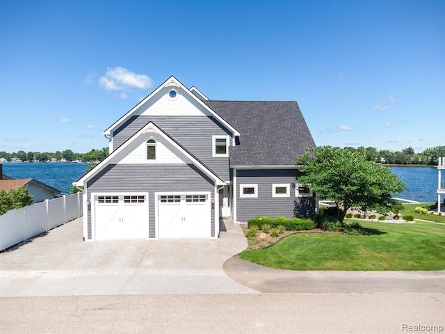 view of front of house with an attached garage, a water view, fence, concrete driveway, and a front lawn