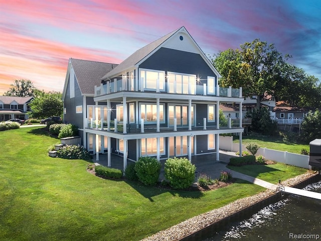 rear view of property featuring a lawn, a balcony, a water view, fence, and a patio area