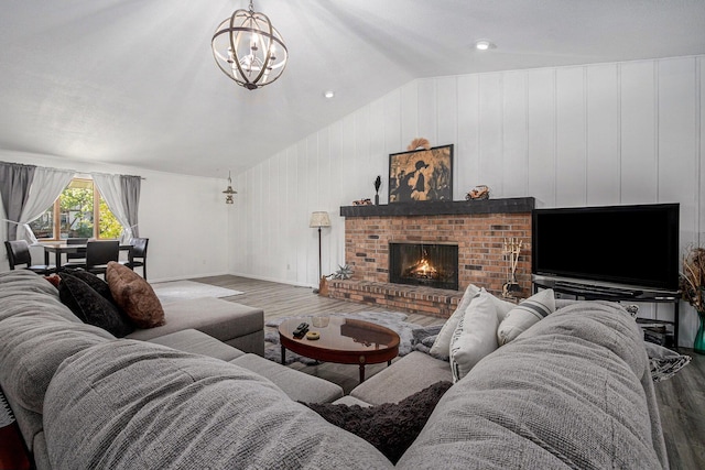 living room with hardwood / wood-style flooring, a chandelier, vaulted ceiling, and a brick fireplace