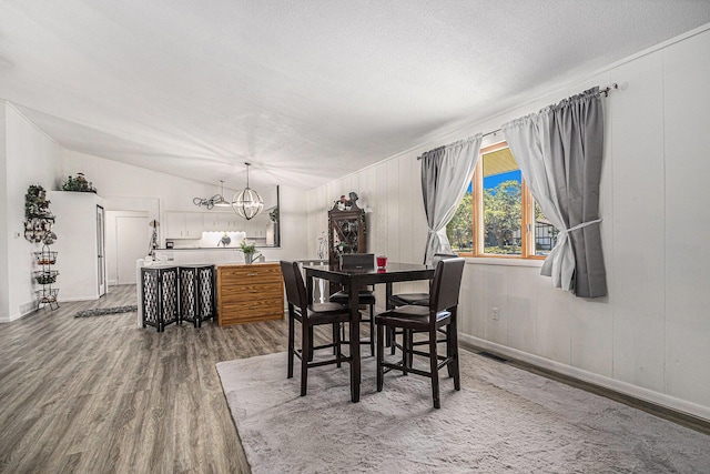 dining room with an inviting chandelier, lofted ceiling, hardwood / wood-style floors, and a textured ceiling