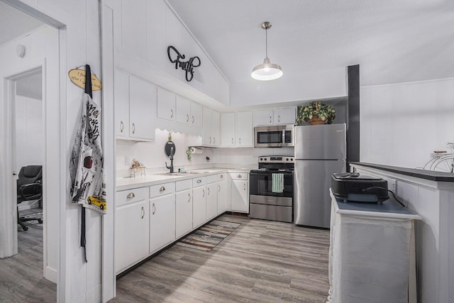 kitchen with sink, wood-type flooring, appliances with stainless steel finishes, pendant lighting, and white cabinets