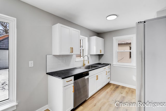 kitchen with appliances with stainless steel finishes, white cabinetry, sink, decorative backsplash, and light wood-type flooring