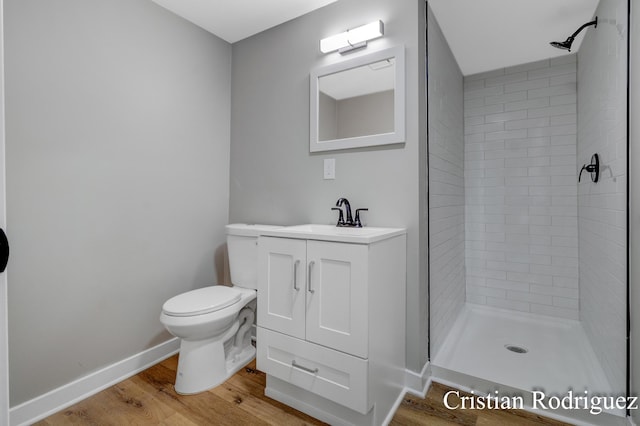 bathroom with hardwood / wood-style flooring, vanity, toilet, and a tile shower