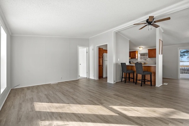 living room featuring lofted ceiling, ornamental molding, ceiling fan, light hardwood / wood-style floors, and a textured ceiling