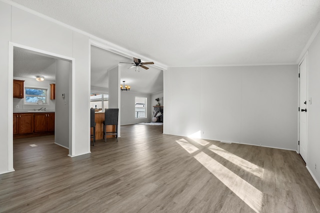 unfurnished living room with hardwood / wood-style flooring, ornamental molding, ceiling fan with notable chandelier, and a textured ceiling