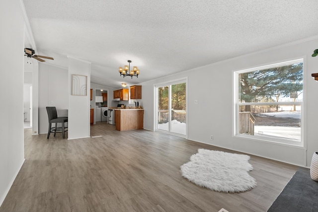 unfurnished living room featuring light hardwood / wood-style flooring, ornamental molding, a textured ceiling, ceiling fan with notable chandelier, and vaulted ceiling