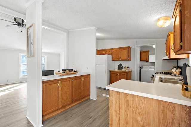 kitchen with ornamental molding, kitchen peninsula, white fridge, washer / clothes dryer, and light hardwood / wood-style floors