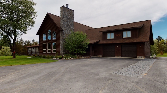 view of front of home with driveway, a front lawn, a chimney, and an attached garage