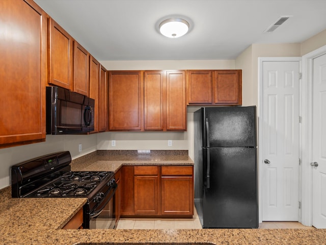 kitchen featuring stone counters, light tile patterned floors, and black appliances