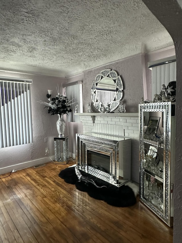 interior details with a brick fireplace, wood-type flooring, ornamental molding, and a textured ceiling