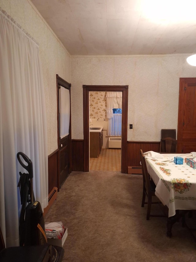 carpeted dining space featuring radiator, a baseboard radiator, and wood walls