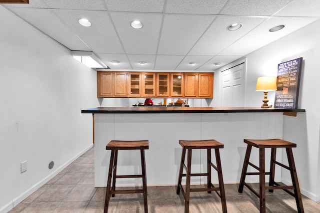 kitchen featuring light tile patterned floors, a paneled ceiling, a kitchen breakfast bar, and kitchen peninsula