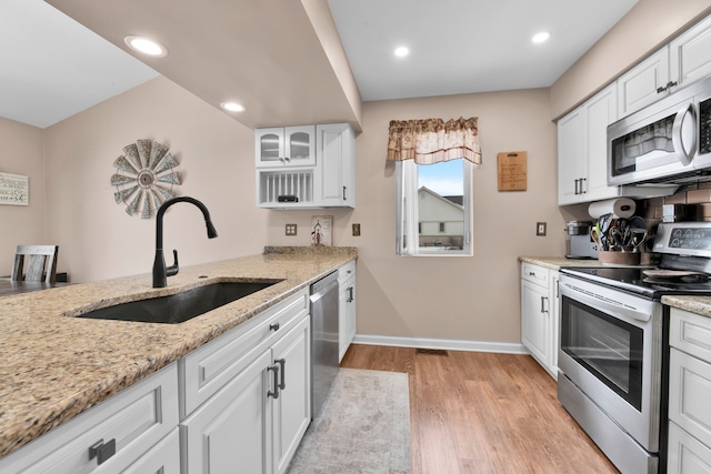 kitchen with sink, white cabinetry, light wood-type flooring, appliances with stainless steel finishes, and light stone countertops