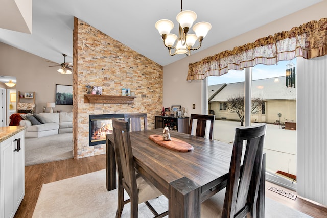 dining room featuring hardwood / wood-style flooring, vaulted ceiling, ceiling fan with notable chandelier, and a fireplace