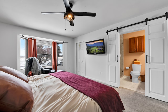 bedroom with ceiling fan, light colored carpet, a barn door, and ensuite bath