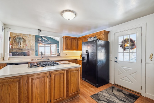 kitchen featuring sink, a center island, light wood-type flooring, pendant lighting, and black appliances