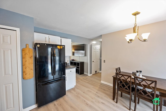 kitchen featuring white cabinetry, hanging light fixtures, a notable chandelier, light hardwood / wood-style floors, and black fridge