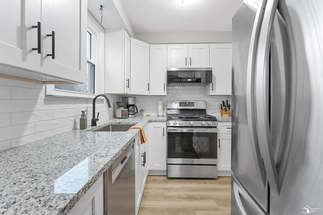 kitchen with sink, appliances with stainless steel finishes, white cabinetry, light stone countertops, and light wood-type flooring