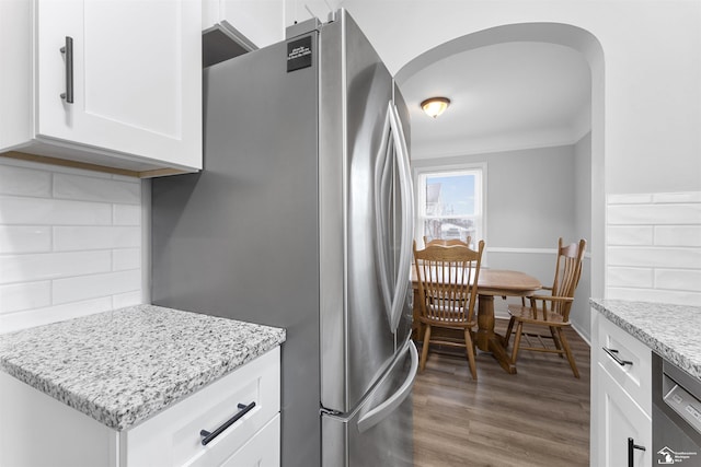 kitchen with hardwood / wood-style floors, white cabinetry, dishwasher, stainless steel fridge, and light stone counters