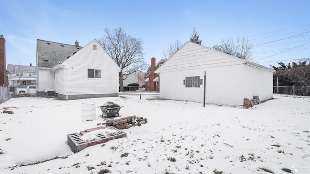 snow covered back of property with cooling unit and an outdoor fire pit