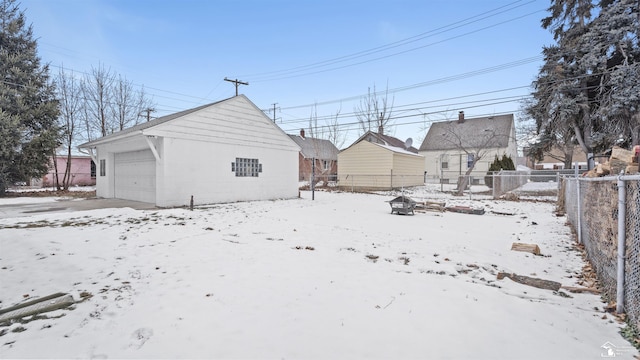 snow covered back of property with a fire pit, a garage, and an outdoor structure