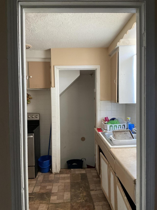 kitchen featuring sink, a textured ceiling, tile walls, electric stove, and washer / clothes dryer