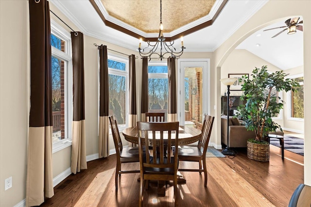 dining space featuring crown molding, hardwood / wood-style floors, a tray ceiling, and ceiling fan with notable chandelier