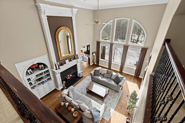 living room featuring hardwood / wood-style flooring, ceiling fan, ornamental molding, and a high ceiling