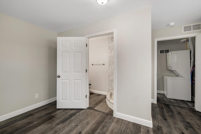 bedroom featuring dark wood-type flooring, ensuite bathroom, and stacked washing maching and dryer