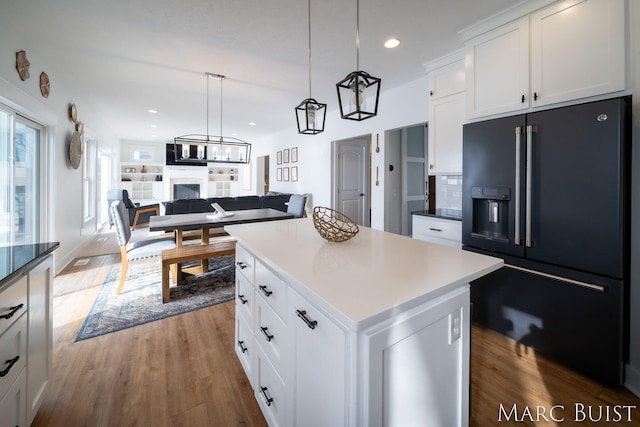 kitchen with black fridge, wood-type flooring, decorative light fixtures, a kitchen island, and white cabinets