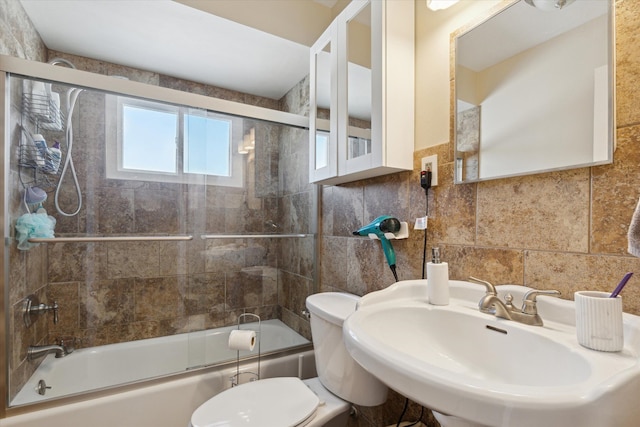 full bathroom with combined bath / shower with glass door, sink, tile walls, and toilet