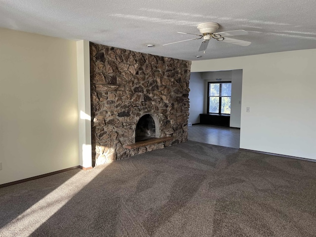 unfurnished living room with ceiling fan, a stone fireplace, a textured ceiling, and dark colored carpet