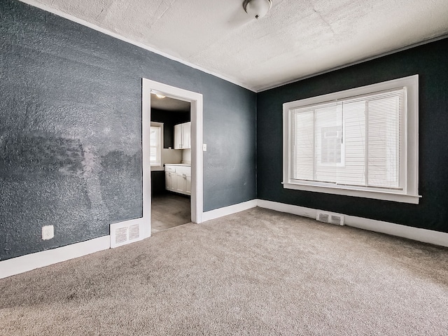 unfurnished bedroom with ensuite bathroom, a textured ceiling, and carpet flooring