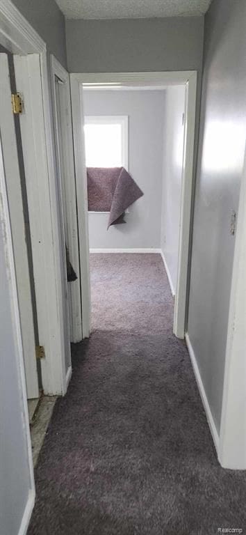 hall with a textured ceiling and dark carpet