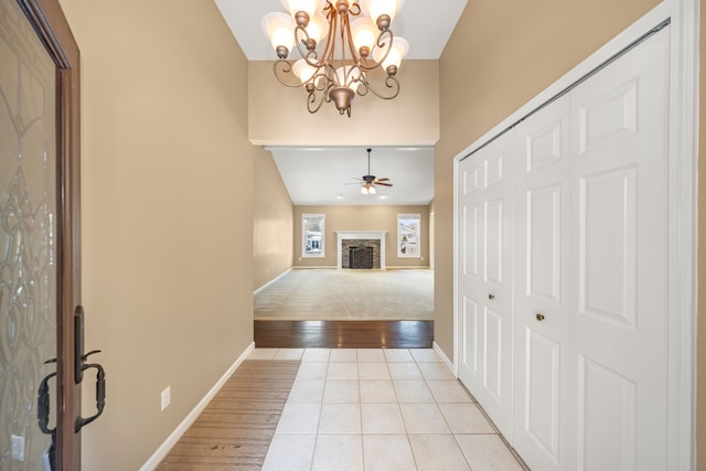 foyer with light tile patterned floors, a stone fireplace, ceiling fan with notable chandelier, and baseboards