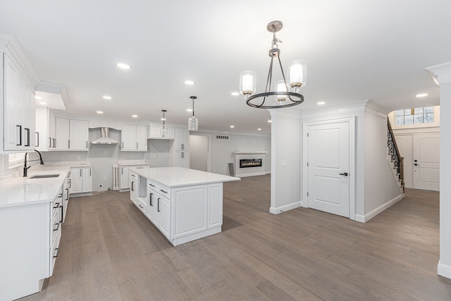 kitchen with sink, white cabinets, hanging light fixtures, a center island, and wall chimney range hood