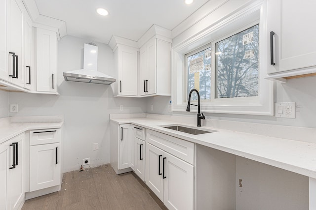 kitchen featuring white cabinetry, sink, light stone countertops, wall chimney range hood, and light hardwood / wood-style flooring