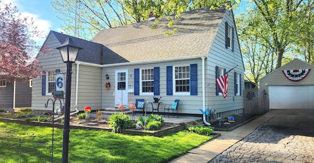 view of front of house featuring a front lawn, an outbuilding, roof with shingles, and a garage
