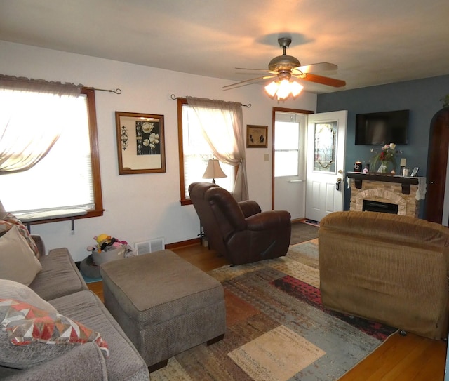 living room featuring ceiling fan, a fireplace, visible vents, and wood finished floors