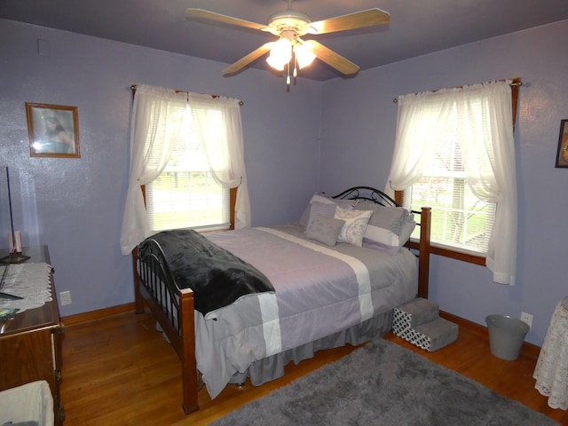 bedroom featuring multiple windows, baseboards, wood finished floors, and a ceiling fan