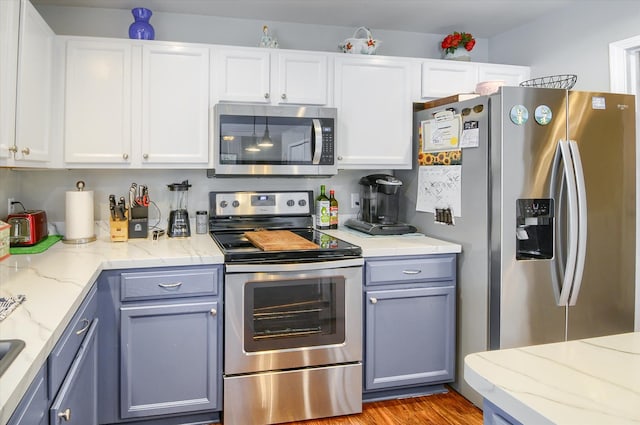 kitchen with light stone counters, light hardwood / wood-style flooring, white cabinets, and appliances with stainless steel finishes