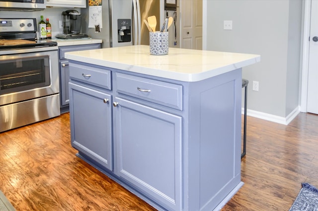 kitchen featuring appliances with stainless steel finishes, a center island, light stone countertops, blue cabinets, and dark hardwood / wood-style flooring