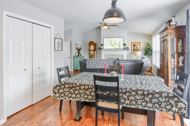 dining room with lofted ceiling, wood-type flooring, a tile fireplace, and ceiling fan