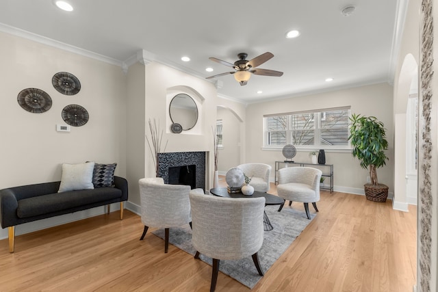 living room featuring a tile fireplace, crown molding, ceiling fan, and light hardwood / wood-style floors