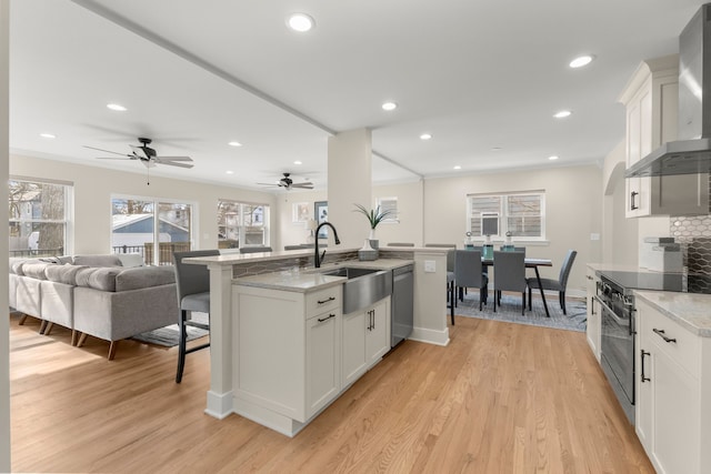 kitchen with sink, wall chimney range hood, white cabinets, and appliances with stainless steel finishes