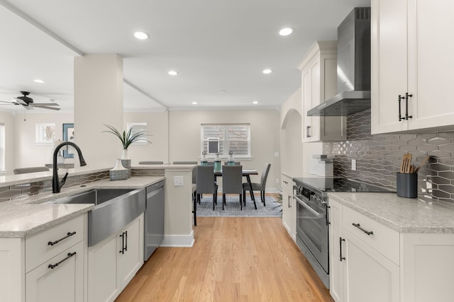 kitchen featuring wall chimney range hood, sink, white cabinetry, stainless steel appliances, and light stone countertops