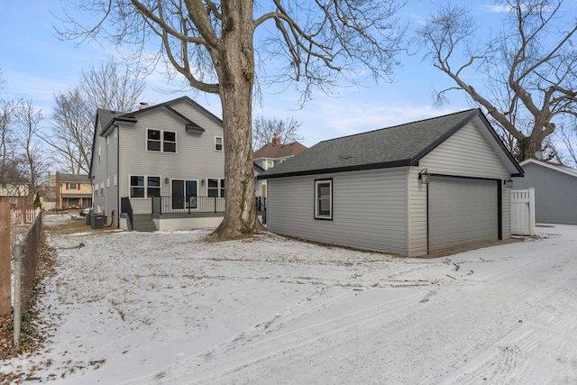 snow covered rear of property featuring a garage and cooling unit