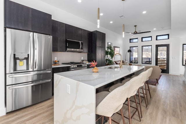 kitchen with a kitchen bar, sink, appliances with stainless steel finishes, an island with sink, and pendant lighting