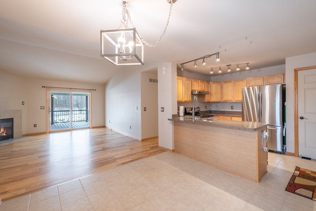 kitchen featuring stainless steel refrigerator, a tiled fireplace, a notable chandelier, light brown cabinetry, and decorative light fixtures