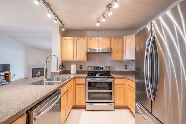 kitchen featuring appliances with stainless steel finishes, light brown cabinetry, sink, and a tile fireplace